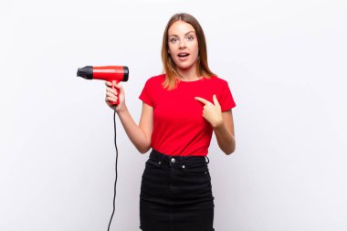 Kızıl saçlı, güzel bir kadın ağzı açık, şaşkın ve şaşırmış bir şekilde bir kuaförü elinde tuttuğunu gösteriyor.