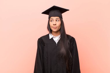 Genç Latin kız öğrenci merak ediyor, mutlu düşünceler ve fikirler düşünüyor, hayal kuruyor, kenarda yer arıyor.