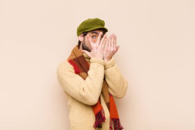 Genç havalı sakallı adam korkmuş ya da utanmış hissediyor, gözleri yarı kapalı ya da elleri kapalı dikizliyor ya da gözetliyor.