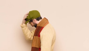 Genç havalı sakallı adam stresli ve endişeli, bunalımda ve hayal kırıklığına uğramış hissediyor, iki elini de başa kaldırıyor.