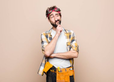 young housekeeper man thinking, feeling doubtful and confused, with different options, wondering which decision to make against flat wall