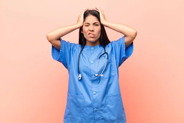 young latin nurse feeling frustrated and annoyed, sick and tired of failure, fed-up with dull, boring tasks against pink wall