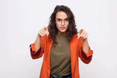 Genç ve güzel bir kadın kameraya iki parmağını ve kızgın bir ifadeyle bakıyor ve sana beyaz duvara karşı görevini yapmanı söylüyor.