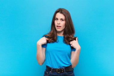 Genç, güzel bir kadın kendini mutlu, şaşırmış ve gururlu hissediyor. Heyecanlı ve şaşkın bir şekilde mavi duvara bakıyor.