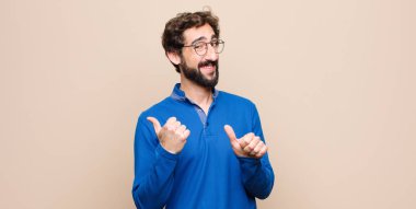 Genç yakışıklı adam neşeyle gülümsüyor ve yan taraftaki fotokopi alanını gösteriyor, düz duvara karşı mutlu ve tatmin olmuş hissediyor.