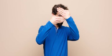 Genç yakışıklı adam kameraya hayır diyen iki eliyle yüzünü kapatıyor! Resimleri reddetmek ya da yasaklı fotoğrafları düz duvara yaslamak