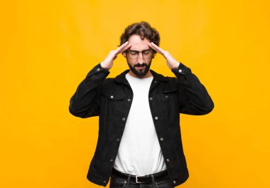 Genç çılgın yakışıklı adam konsantre, düşünceli ve ilham verici görünüyor, beyin fırtınası yapıyor ve elleri turuncu duvarda hayal ediyor.