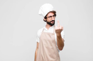 Genç çılgın şef kızgın, sinirli, asi ve agresif hissediyor, orta parmağını sallıyor, beyaz duvara karşı savaşıyor.
