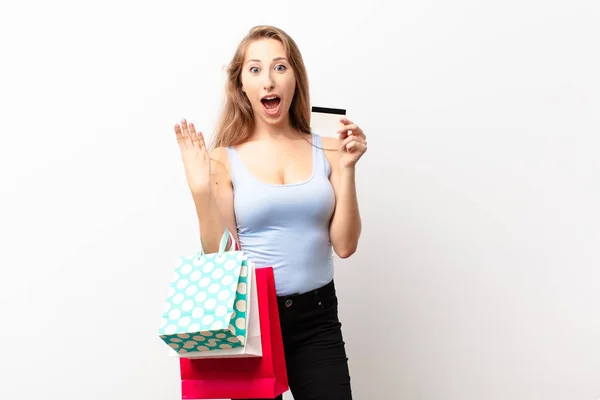 若いブロンドの女性は笑顔でフレンドリーに見える前方に手で4番目または4番目を示しショッピングバッグを持ってカウントダウン — ストック写真