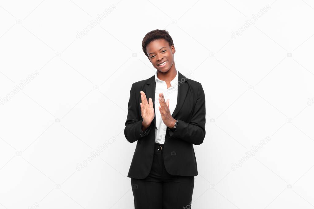 young pretty black womanfeeling happy and successful, smiling and clapping hands, saying congratulations with an applause against white wall