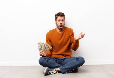 Genç, yakışıklı, ağzı açık ve şaşırmış, şaşırmış ve şaşırmış bir şekilde elinde dolar banknotları tutarak inanılmaz bir sürpriz yapmış. 
