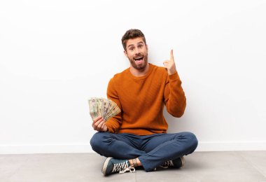 Genç yakışıklı bir adam bir fikri fark ettikten sonra mutlu ve heyecanlı bir dahi gibi hissediyor, neşeli bir şekilde parmağını kaldırıyor, eureka! Dolar banknotları tutuyordu 