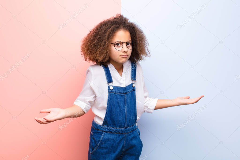 african american little girl feeling clueless and confused, having no idea, absolutely puzzled with a dumb or foolish look against flat wall