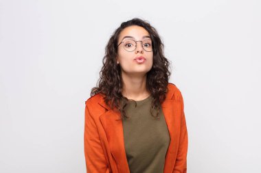 Genç, güzel bir kadın dudaklarını birbirine bastırıyor tatlı, eğlenceli, mutlu, sevimli bir yüz ifadesiyle, beyaz duvara bir öpücük yolluyor.