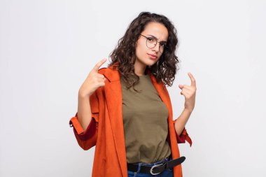 Kötü tavırlı genç ve güzel bir kadın gururlu ve agresif görünüyor, yukarı bakıyor ya da beyaz duvara yaslanmış ellerle alay ediyor.