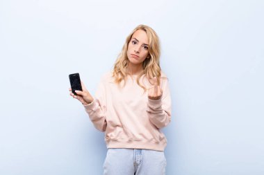 Genç sarışın kadın kızgın, sinirli, isyankar ve agresif hissediyor, orta parmağını hareket ettiriyor, akıllı telefon kullanarak karşılık veriyor.