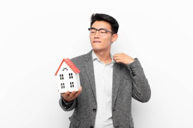 Genç Japon bir adam stresli, endişeli, yorgun ve hayal kırıklığına uğramış, gömleğini çekiştiren, bir ev modelinden rahatsız olmuş gibi görünüyor.