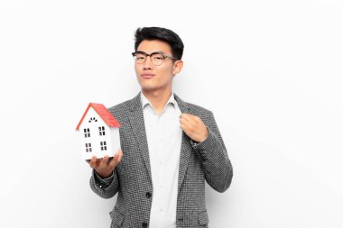 Genç Japon adam kibirli, başarılı, pozitif ve gururlu görünüyor, bir ev modeliyle kendini işaret ediyor.
