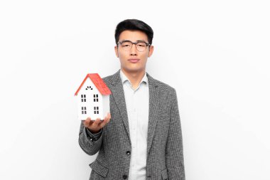 Genç Japon bir adam üzgün ve mızmızlanıyor, mutsuz bir bakışla, negatif ve hayal kırıklığına uğramış bir ev modeli ile ağlıyor.