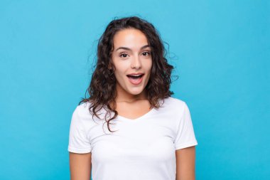 Genç ve güzel bir kadın çok şaşırmış ya da şaşkın görünüyor, ağzı açık mavi arka plana karşı 