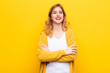 Genç, güzel, sarışın bir kadın mutlu, gururlu ve memnun görünüyor. Kollarını sarı duvara dolamış başarıyla gülümsüyor.