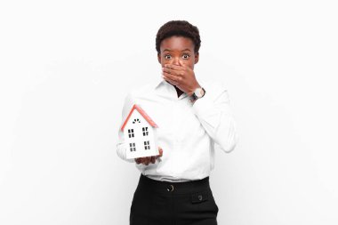 Şok olmuş, şaşırmış bir ifadeyle elleri olan, genç ve güzel siyahi bir kadın bir sır saklıyor ya da bir ev modeliyle 