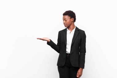 Genç, siyah bir kadın mutlu ve gülümsüyor. Beyaz duvara karşı elde tutulan bir nesneye ya da konsepte bakıyor.