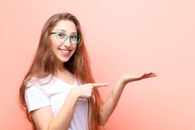 Genç sarışın kadın neşeyle gülümsüyor ve yan taraftaki fotokopi alanına işaret ediyor, bir nesneyi gösteriyor veya reklamını yapıyor.