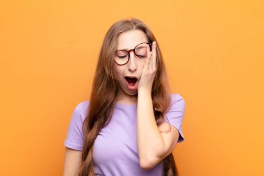 Genç sarışın kadın uykulu, sıkılmış ve esniyor, baş ağrısı ve yüzünün yarısını kaplayan bir eliyle