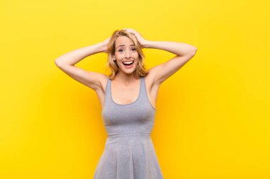 Genç sarışın kadın mutlu, kaygısız, arkadaş canlısı ve rahat görünüyor. Turuncu duvara karşı pozitif bir tavırla hayattan ve başarıdan zevk alıyor.