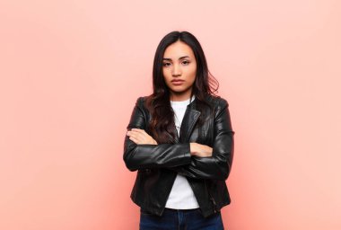 Genç, Latin, güzel bir kadın hayal kırıklığına uğramış ve hayal kırıklığına uğramış, ciddi görünüyor, kızgın ve kolları düz duvara dayalı.