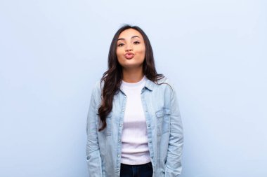 Tatlı, eğlenceli, mutlu, sevimli bir yüz ifadesiyle dudaklarını birbirine bastıran genç Latin, güzel bir kadın, düz duvara bir öpücük yolluyor.