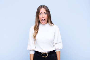 Genç, güzel İspanyol kadın korkmuş ve şok olmuş hissediyor, ağzı açık, mavi duvara karşı şaşkınlık içinde.