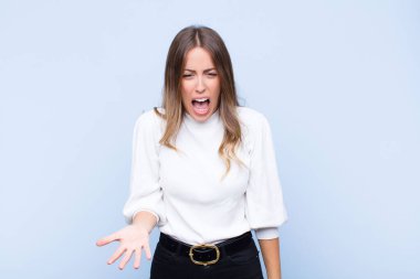 Genç, güzel, İspanyol bir kadın sinirli, sinirli ve sinirli görünüyor. Mavi duvara karşı senin neyin var? 