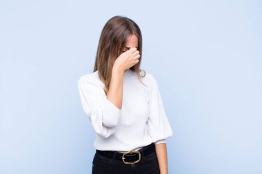 Genç ve güzel İspanyol kadın stresli, mutsuz ve hayal kırıklığına uğramış, alnına dokunuyor ve mavi duvara karşı şiddetli baş ağrısı çekiyor.