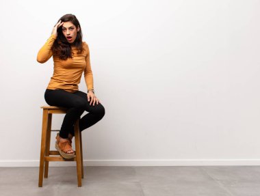 Genç ve güzel bir kadın kameraya iki parmağıyla ve kızgın bir ifadeyle bakıp bir odada oturarak görevini yapmanı söylüyor.