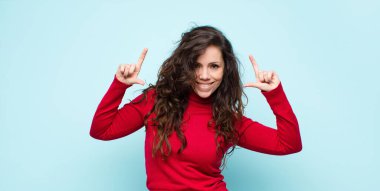 Genç, güzel bir kadın iki eliyle kendi gülümsemesini çiziyor, olumlu ve mutlu görünüyor, mavi duvara karşı sağIık kavramı.