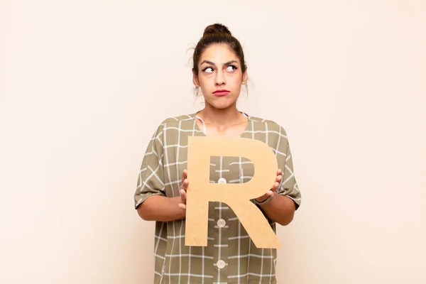 若い女性は混乱し疑わしい考えアルファベットのRという文字を持っていて単語や文を形成しました — ストック写真