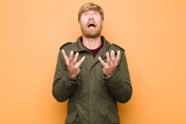 Genç sarışın adam umutsuz ve hayal kırıklığına uğramış görünüyor, stresli, mutsuz ve sinirli, bağırıyor ve düz duvara karşı bağırıyor.