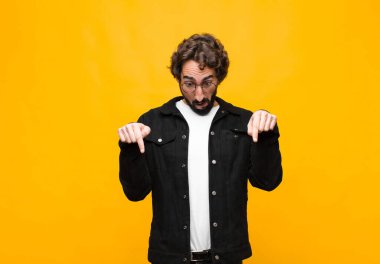 Genç, deli, yakışıklı ve ağzı açık bir adam iki eliyle aşağıya bakıyor. Şaşırmış, şaşırmış ve turuncu duvara bakıyor.