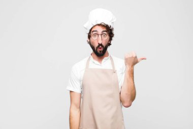 Genç çılgın aşçı inançsızlıktan şaşkın şaşkın bakıyor, yan taraftaki objeyi işaret ediyor ve diyor ki vay be, beyaz duvara karşı inanılmaz.