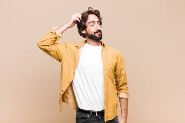 Kafası karışmış, kafası karışmış, başını kaşıyan ve düz duvara bakan genç çılgın adam.