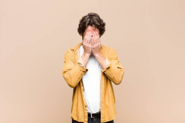 Genç, çılgın, havalı bir adam üzgün, hayal kırıklığına uğramış, gergin ve depresif, iki eliyle yüzünü kaplayan, yassı duvara karşı ağlayan