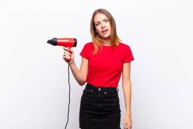 red head pretty woman feeling puzzled and confused, with a dumb, stunned expression looking at something unexpected holding a hairdresser