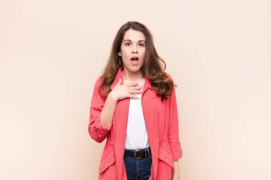 Genç, güzel bir kadın şok olmuş, şaşırmış ve şaşırmış hissediyor, elleri göğsünde ve ağzı açık, kim diyor, ben mi? bej arkaplan