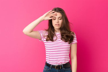 Genç, güzel bir kadın stresli, yorgun ve hayal kırıklığına uğramış görünüyor. Alnından ter akıyor. Pembe duvara karşı umutsuz ve bitkin hissediyor.