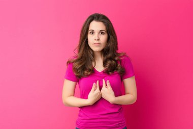 Genç ve güzel bir kadın, şaşkın ve tuhaf bakışlarıyla kendini işaret ediyor. Pembe duvara karşı seçildiği için şaşırmış ve şaşırmış.