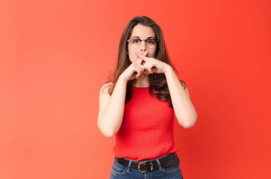Genç ve güzel bir kadın ciddi ve hoşnutsuz görünüyor. Reddedilmek için iki parmağını öne uzatıyor ve kırmızı duvara karşı sessizlik istiyor.
