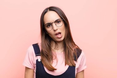 Genç ve güzel bir kadın şaşkın ve şaşkın hissediyor, aptal, şaşkın bir yüz ifadesiyle beklenmeyen bir şeye bakıyor pembe duvara karşı.