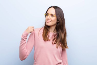 Genç, güzel bir kadın kibirli, başarılı, pozitif ve gururlu görünüyor, kendini mavi duvara gösteriyor.